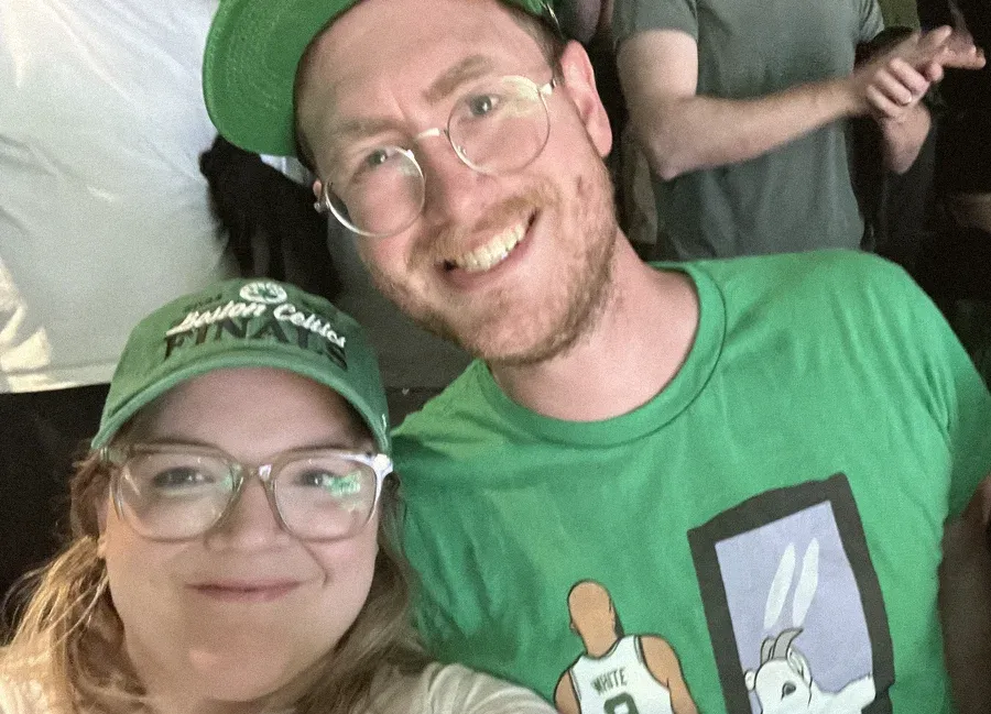 Jordan and her husband in Celtics gear, taking a selfie at a game