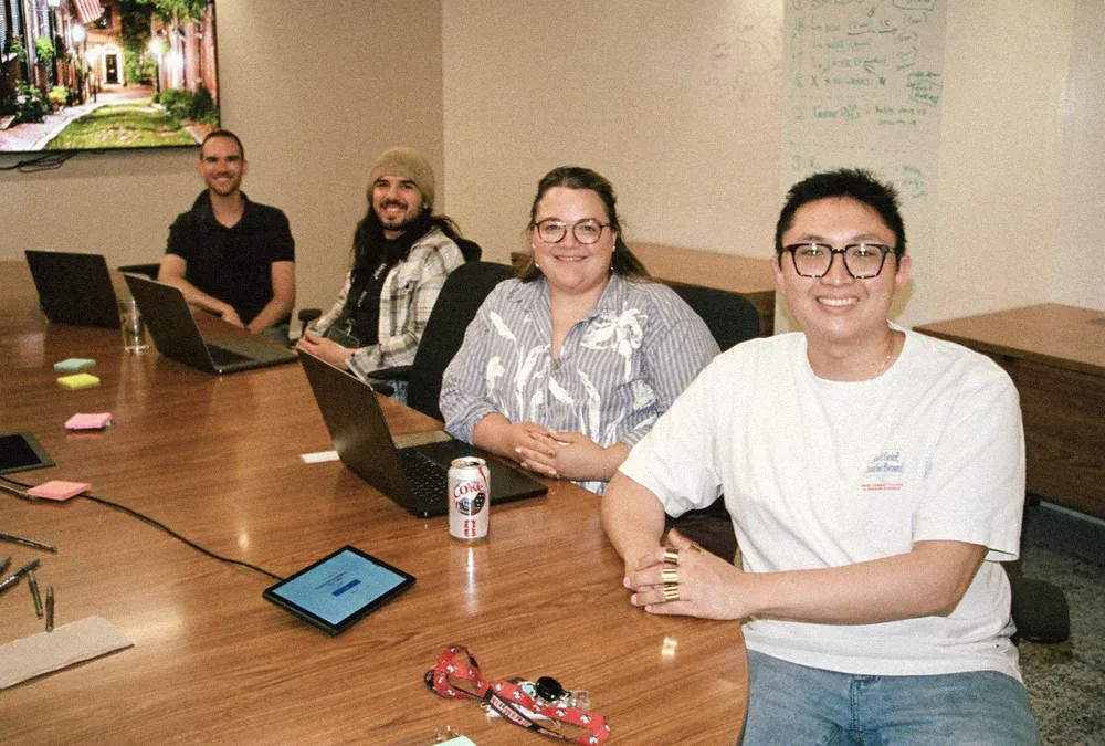 Jordan and three teammates smiling around a conference table with laptops during the internal tools onsite