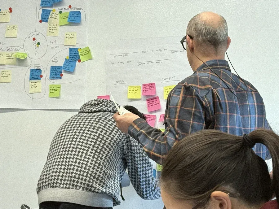 Two designers sorting sticky notes on a wall during a workshop