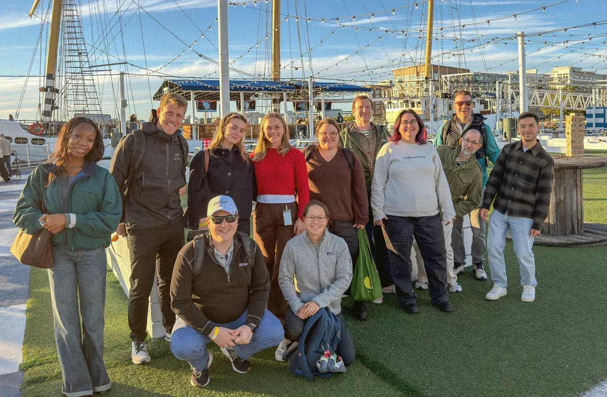 The design team gathered in front of a tall ship on the Boston waterfront